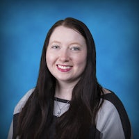 Portrait photo of a smiling white woman with long, straight brown hair and light green eyes, wearing a striped dark and light grey shirt.